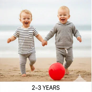 Two toddlers in Aatiyas Fashion clothing playing with a red ball on a sandy beach